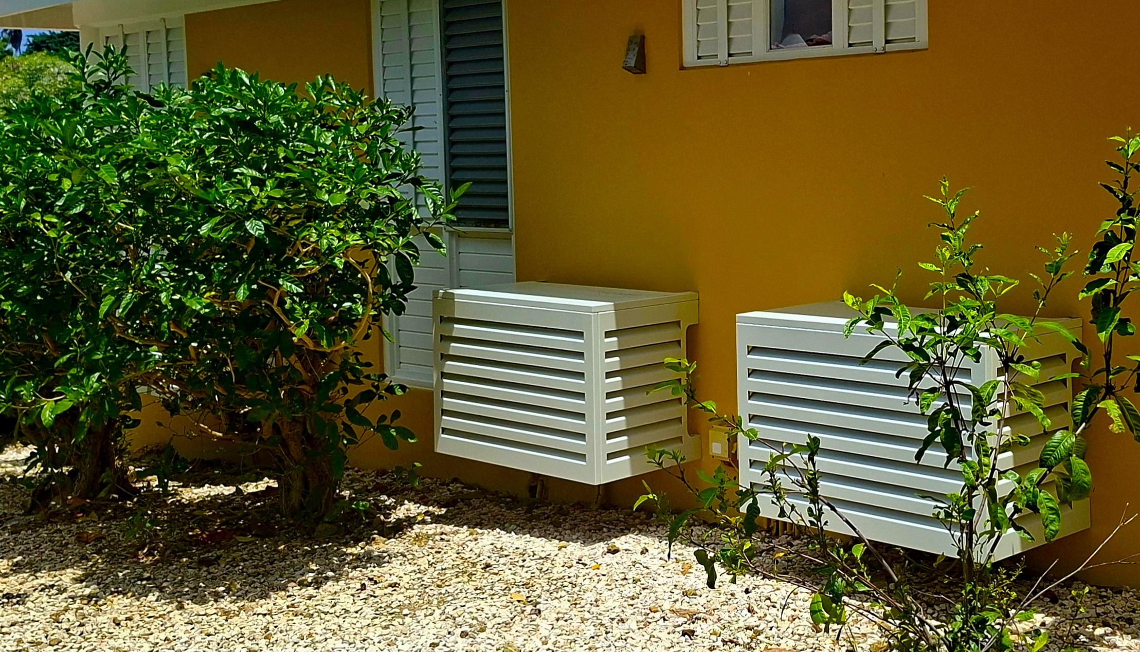 Aluminum airco cover installed along the roofline of a yellow Curacao home