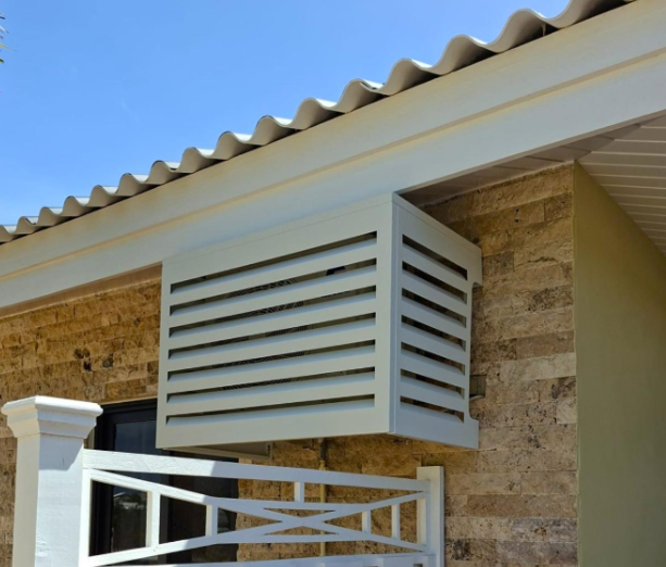 Wall-mounted UnderCovers aluminum AC cover fitted under the eaves of a stone-clad Curacao home